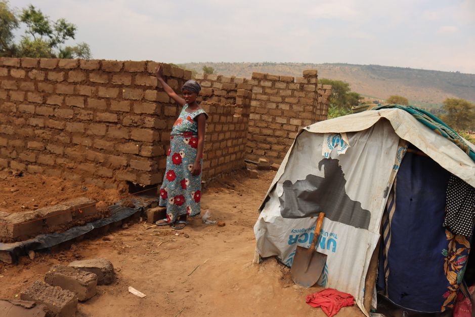 Riziki Angella standing in between her old shelter and the new house