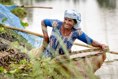 Smilende kvinde i kjole står med fiskenet