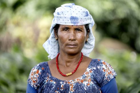 Kvinde iført blå kjole og rød halskæde kigger direkte på kameraet