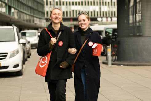 Illustration: Bliv indsamler 12. marts sammen med Folkekirkens Nødhjælp. To kvinder krydser arme med en indsamlingsbøsse i hånden samler ind for Folkekirkens Nødhjælp