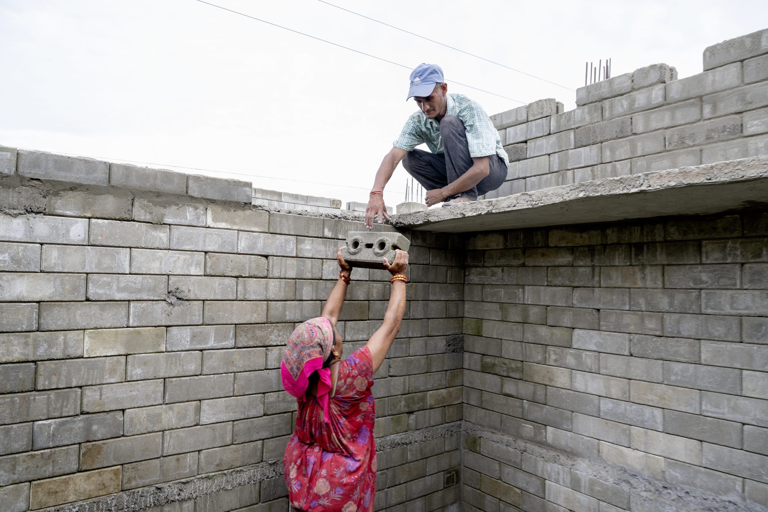 Kvinde iført rød kjole løfter en mursten til en mand