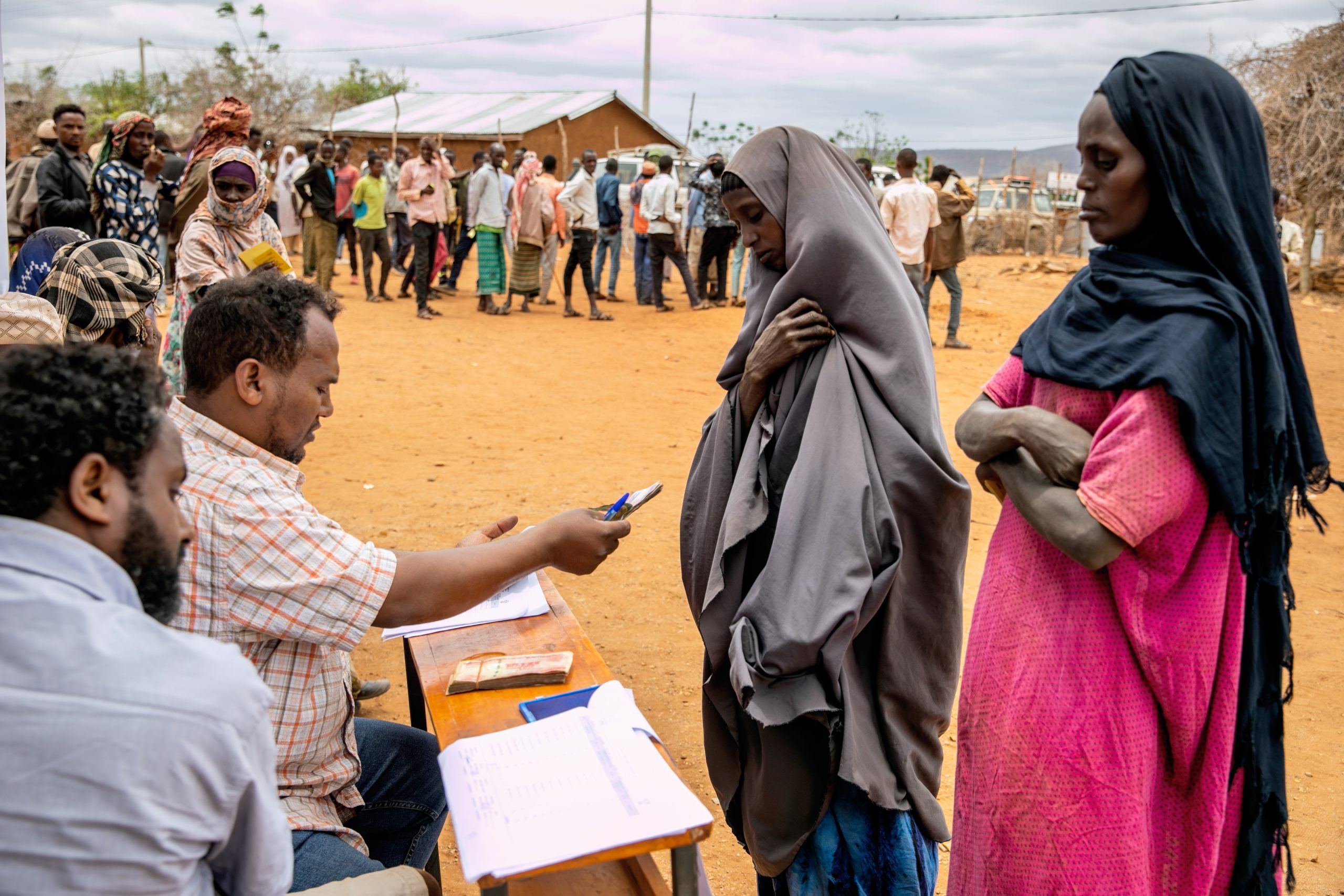 To kvinder står ved en skranke hvor en mand giver den ene kvinde penge