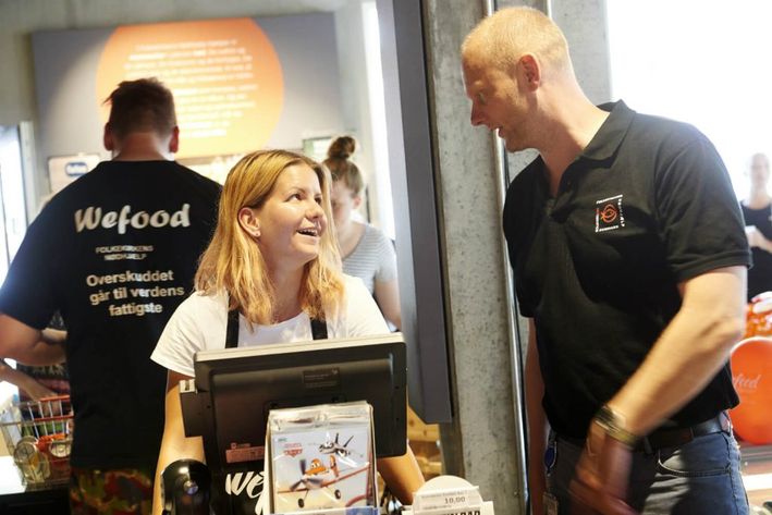 To Wefood-frivillige snakker sammen foran kassen i butikken og er i godt humør.