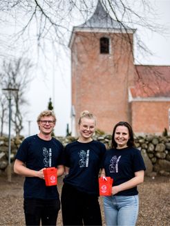 Tre indsamlere fra Folkekirkens Nødhjælp står foran deres lokale kirke.