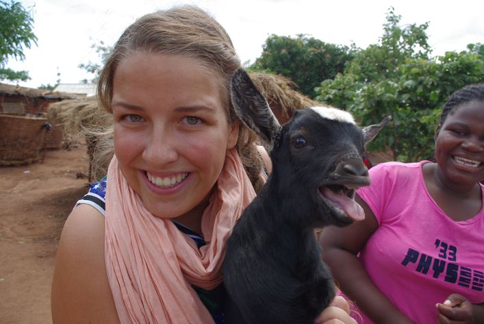 Ung kvinde står med ged i favnen, mens en anden kvinde står bagved og griner