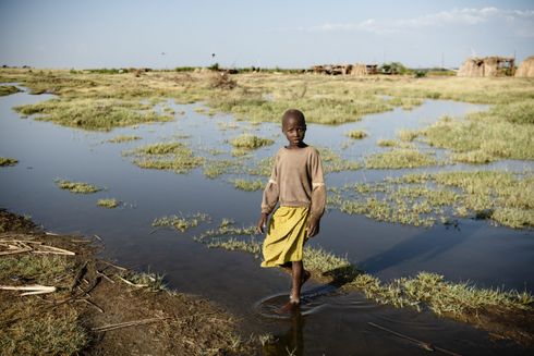 Aminit, pige fra Kenya i gul kjole står i vand. Illustration for klimaforandringer.