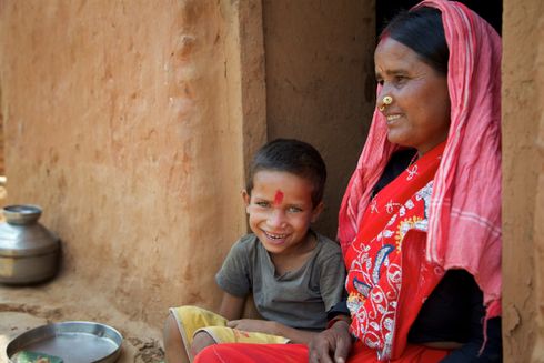 Smilende dreng sidder på skødet af sin mor i Banlek, Nepal