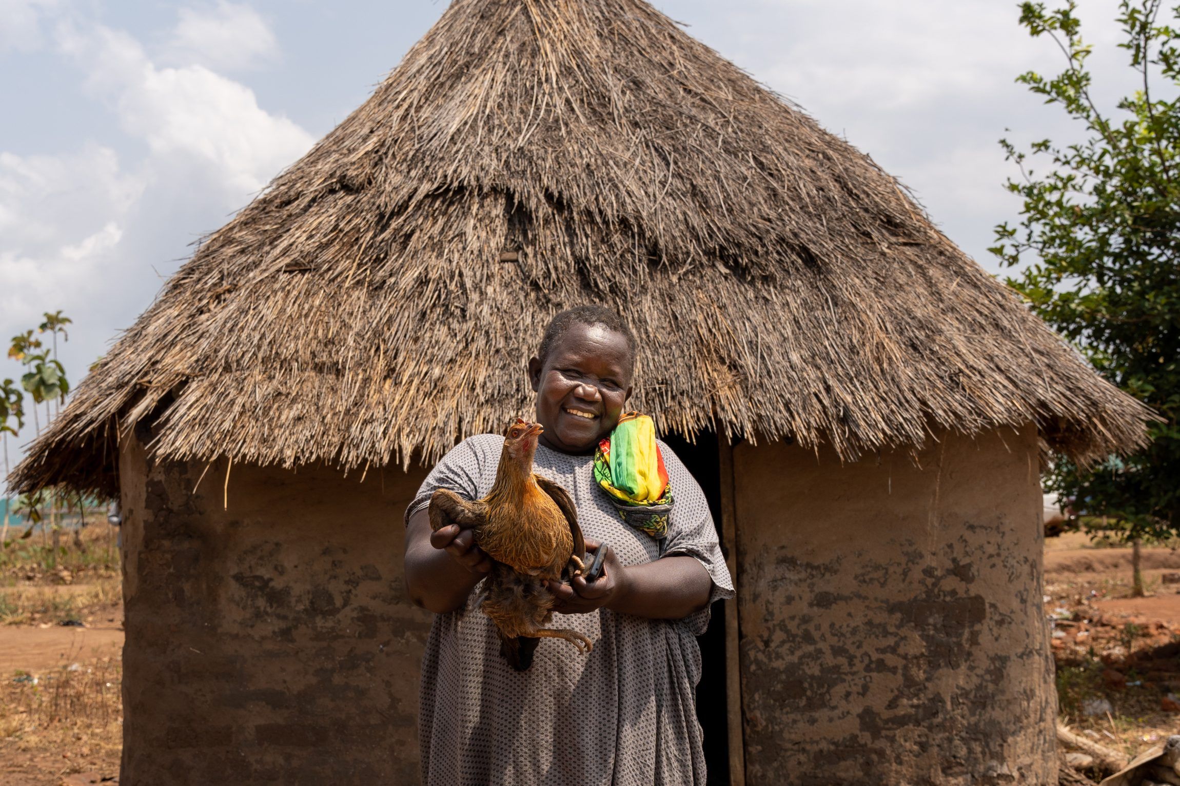 Vickys står med en af hendes kyllinger, som hun sælger. Pengene går til at købe medicin og skolegang for sine tre børn.